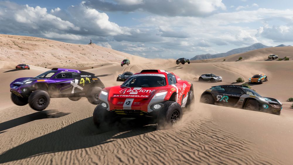 Several Extreme E off-road race cars driving and stunting around the sandy desert.