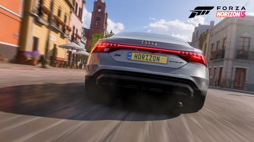 A rear view of the silver 2021 Audi RS e-tron GT as it drives into the city of Guanajuato surrounded by yellow, orange and white historical buildings.
