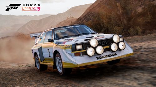 An Audi Sport quattro S1 adorned in a yellow and white livery with the #2 lifts up the dust on a dirt trail.