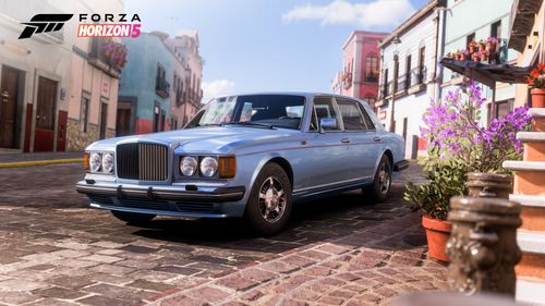A blue 1991 Bentley Turbo R parked by flowerpots and buildings in the colorful city of Guanajuato.