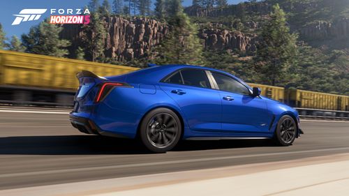 Side view of the blue 2022 Cadillac CT4-V Blackwing as it races alongside a yellow train in the canyon.