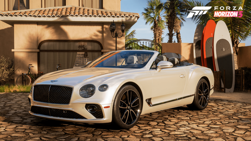 White Bentley Continental with its roof off parked on a stone driveway in front of a house