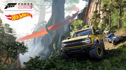 A yellow off-road Ford Bronco with its wheels turned approaches the camera as other cars follow in a dense jungle environment filled with trees and shrubbery. Two tall trees are surrounded by a large, twisting orange track. 