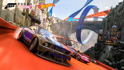 Hot Wheels cars including a purple Ford Mustang and pink Twin Mill race towards the camera. The background features a blue loop-de-loop track going around an archway, while an orange track goes through it. Buildings are attached to the rocky environment s