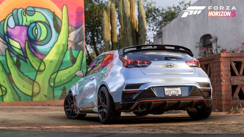 A blue 2019 Hyundai Veloster N featuring the ADRO USA widebody parked by a green Mexican mural.