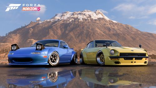 Two Rocket Bunny cars, one blue, the other yellow, parked sideways with reflections underneath in front of the Gran Caldera volcano.