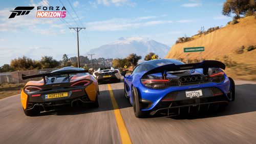 A trio of McLarens, one blue, one white and another grey and orange, drive at speed on a road towards a mountain.