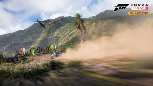 Colin McRae's Ford Focus RS kicks up dust as it blasts down a dirt trail in Sierra Nueva, surrounded by rocky terrain covered in greenery.