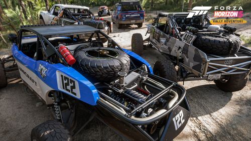 Group of buggies parked on a dirt trail in the palm tree forest. One buggy features a blue and white livery, another features mostly grey tones. Up ahead the blue Ford Lightning can be seen and the orange Hoonigan Baja Beetle.