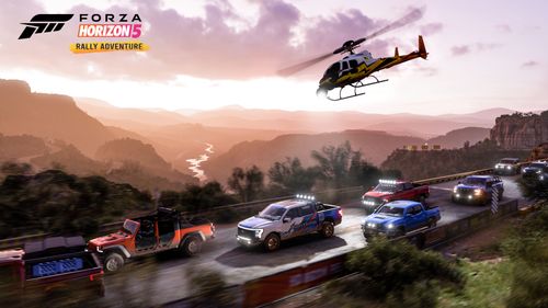 Several vehicles drive across an asphalt road as the sky is filled with pink and orange hues to compliment the sunset. The Horizon Rally Helicopter is flying above the vehicles.