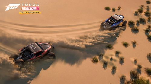 Birds eye view of two buggies creating tire tracks and kicking up massive dust trails in the smooth sandy desert.