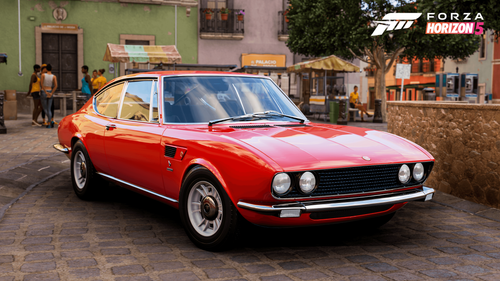 Red Fiat Dino parked in front of a green wall on top of a rocky road