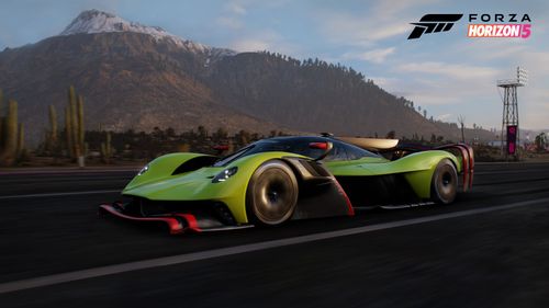 Aston Martin Valkyrie driving on a quiet road with a snow-covered mountain as its backdrop