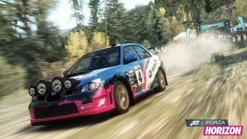 A Subaru rally car with a blue, white and pink livery races through an off-road trail with trees and foliage surrounding it.