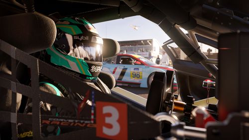 A driver in a cyan coloured race suit and helmet sitting in the 2020 Chevrolet #3 Corvette Racing C8.R with the door open. A blue and red  2020 Hyundai #98 Bryan Herta Autosport Veloster N can also be seen in the background.